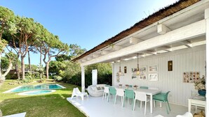 Eine Außenpatio mit Pool, weißer Möbel und einer strohgedeckten Struktur.