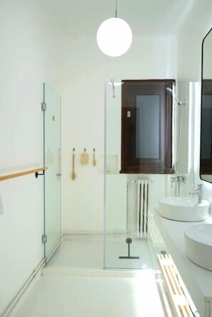 Ein modernes Badezimmer mit einer Duschkabine aus Glas, einer Holzbadematte, einem weißen Waschbecken und einem Spiegel darüber.