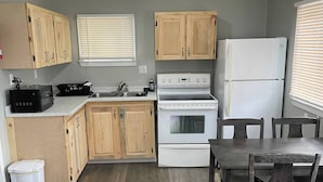 A compact kitchen with wooden cabinets, a white stove, a refrigerator, and a dining table with chairs. - Oakhill Oasis Guest House (Oak Hill)