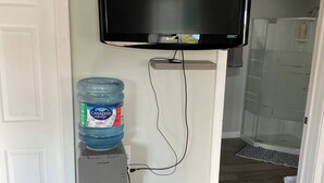 A compact living space with a flat-screen TV mounted on a wall, a water dispenser, and a small refrigerator. - Oakhill Oasis Guest House (Oak Hill)