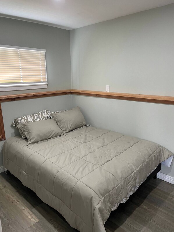 A bedroom with a bed, a window with blinds, and a wooden trim along the ceiling. - Oakhill Oasis Guest House (Oak Hill)