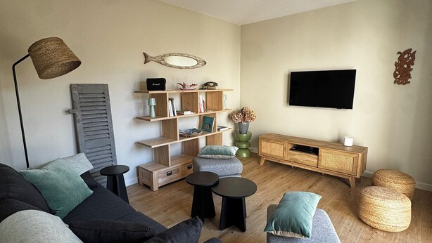 Ein Wohnzimmer mit einer Couch, Sesseln, einem Couchtisch, einem Fernseher, Regalen mit Büchern und Dekoration sowie einem Holzschrank.