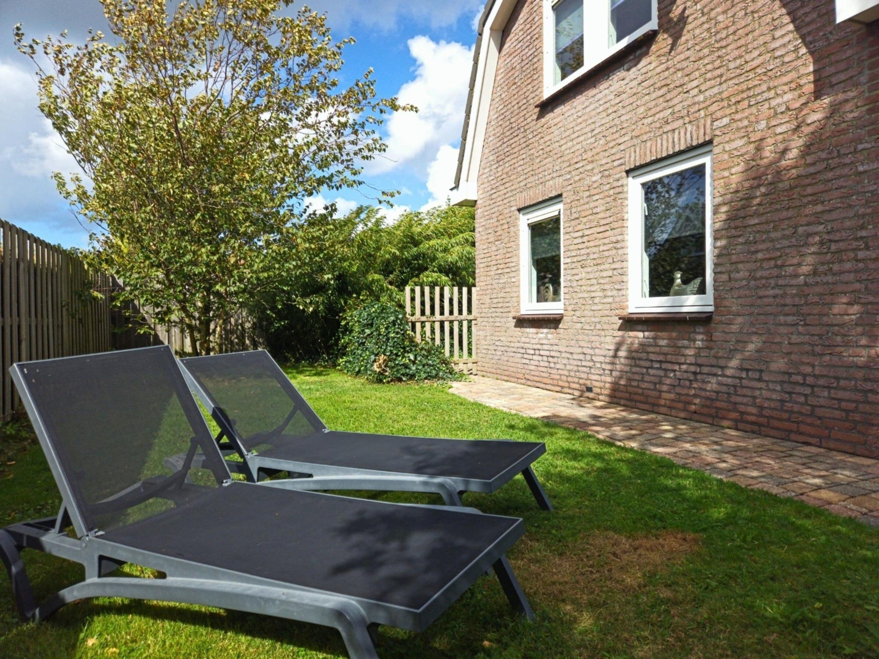Un jardin avec deux chaises longues, une maison en briques et une clôture en bois.