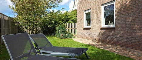 A backyard with two lounge chairs, a brick house, and a wooden fence.