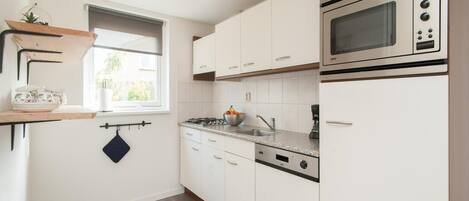 A kitchen with white cabinets, a microwave, a stove, and a window with a view.