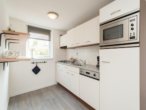 A kitchen with white cabinets, a microwave, a stove, and a window with a view. - Contemporary Family Haven in Noordwijk (Noordwijk)