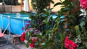A poolside area with a blue pool, a wooden deck, and potted plants with pink flowers. - La casa di Gio'- Apartamento Rustico Legno (CALTANISSETTA)