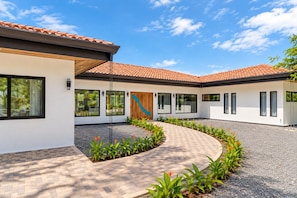 A modern house with a curved driveway, large windows, and a tiled roof. - Hacienda style home 4 bedrooms in Las Golondrinas, Hacienda Pinilla (Pinilla)