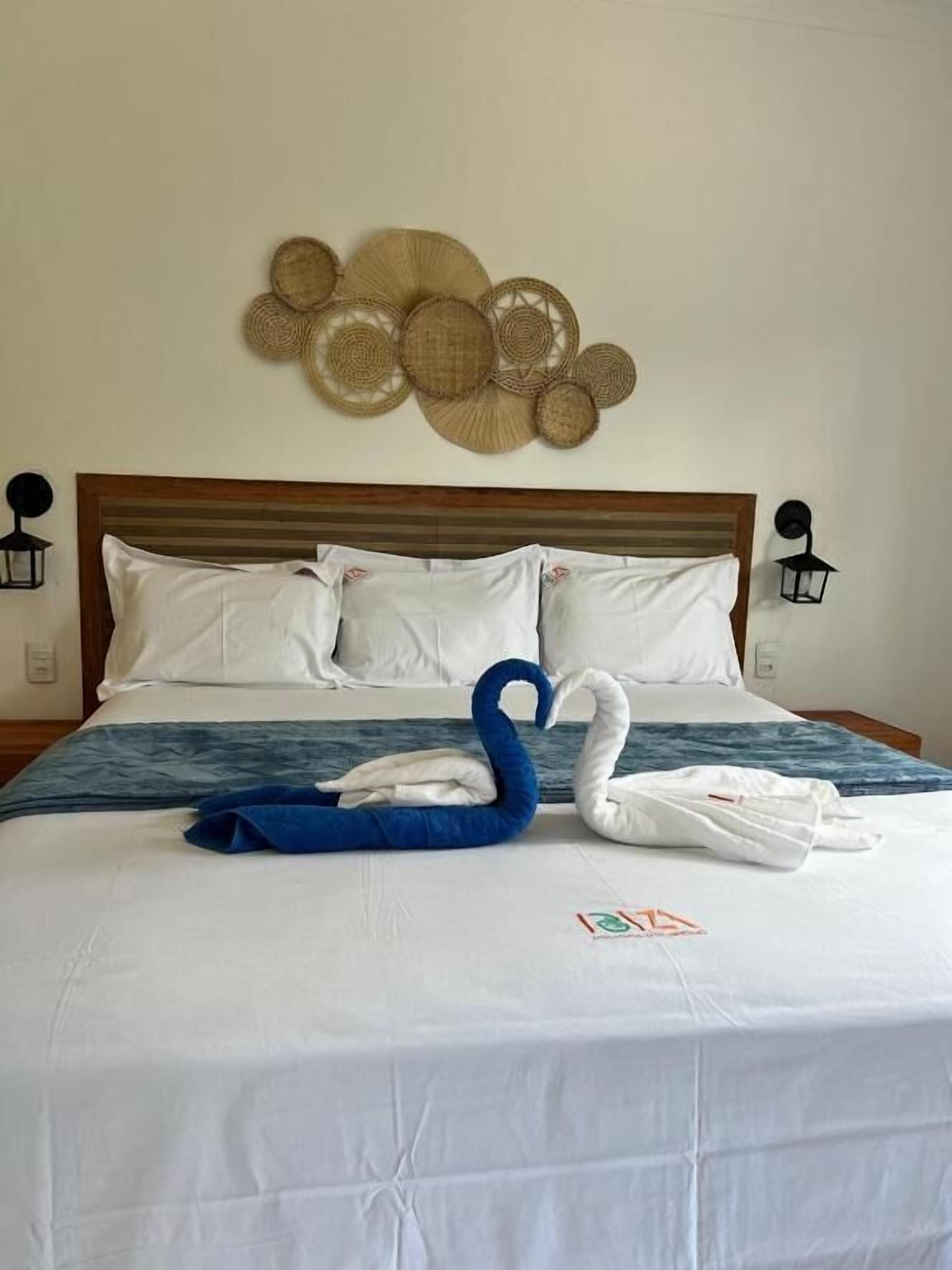 A neatly made bed with white linens and a blue and white swan-shaped towel arrangement.