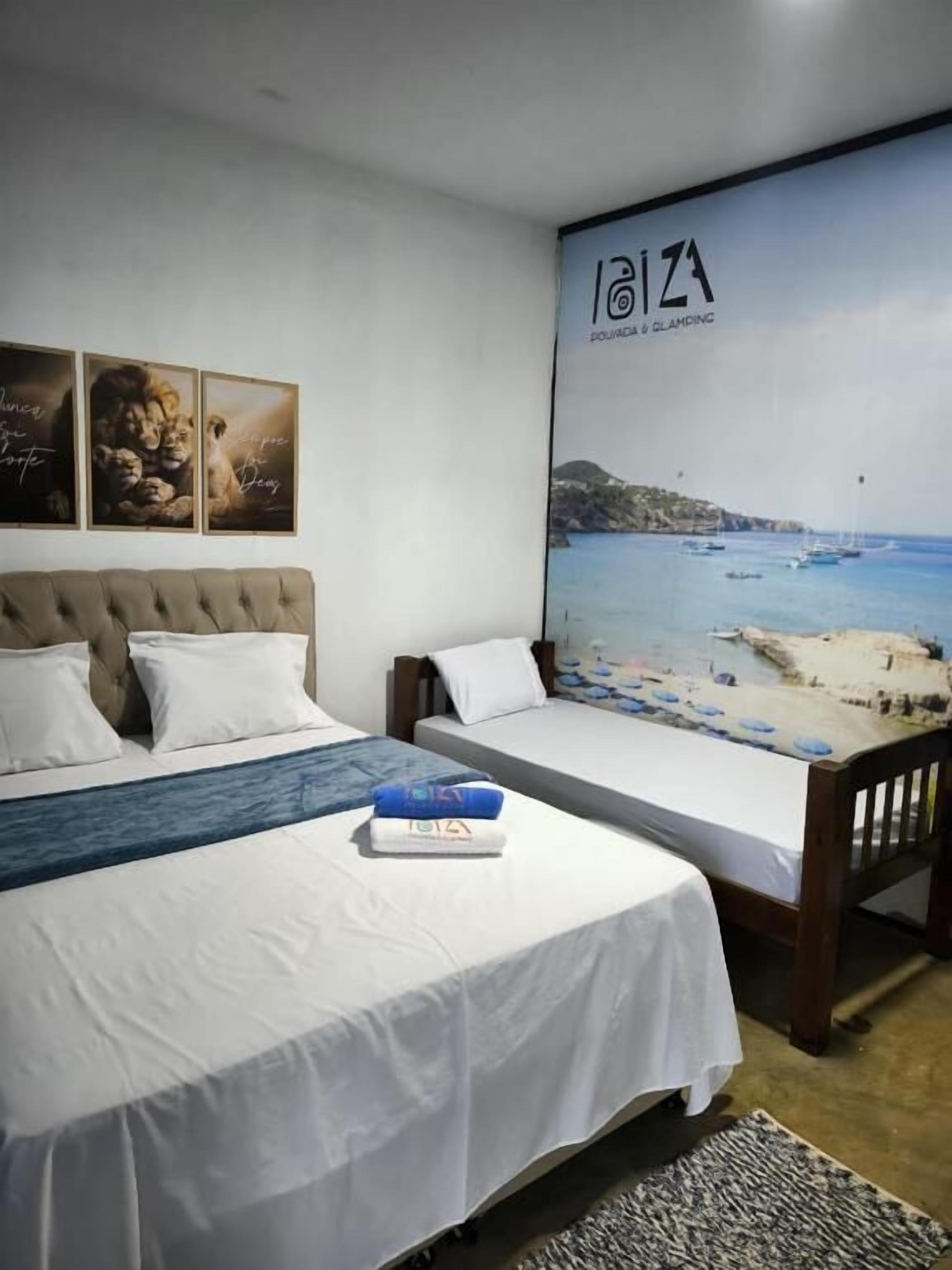A hotel room with two beds, a large poster of a beach scene, and three framed pictures on the wall.