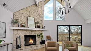 Ein geräumiges Wohnzimmer mit Kamin aus Stein, einem großen Fenster und Blick ins Freie.