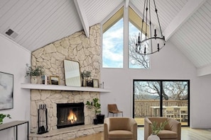 A spacious living room with a stone fireplace, a large window, and a view of the outdoors. - Modern Lakeview Retreat, Beach Club Access with 2 Decks (Lake Arrowhead)