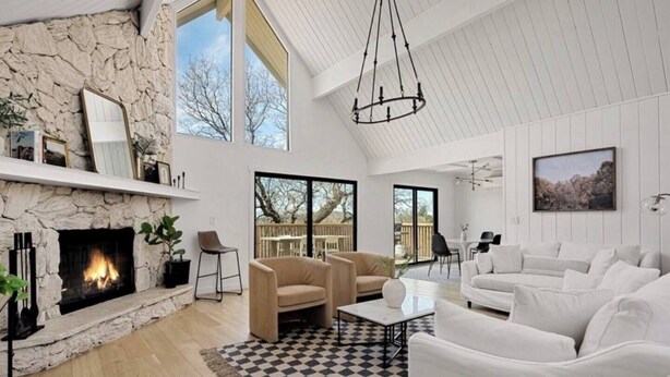 Ein geräumiges Wohnzimmer mit Kamin aus Stein, einem großen Fenster und einer hohen Decke mit freiliegenden Balken.