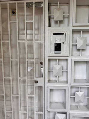 A white, grid-patterned wall with multiple square and rectangular openings, some with handles and others with electrical boxes. - Group Stay 21 Guests, Wifi 900 Mb (Medellín)
