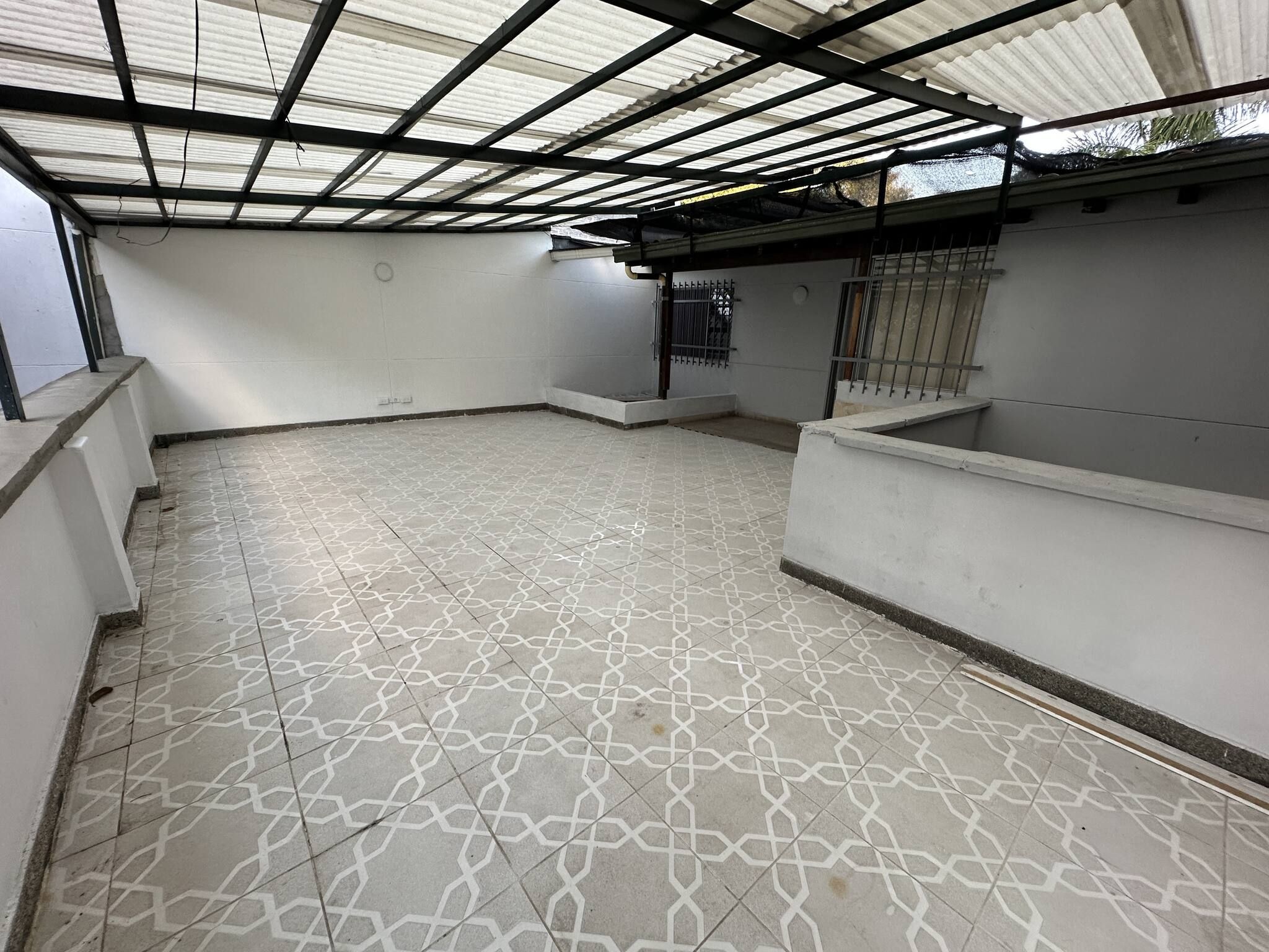 A covered outdoor area with a patterned floor, metal beams, and a window with bars.