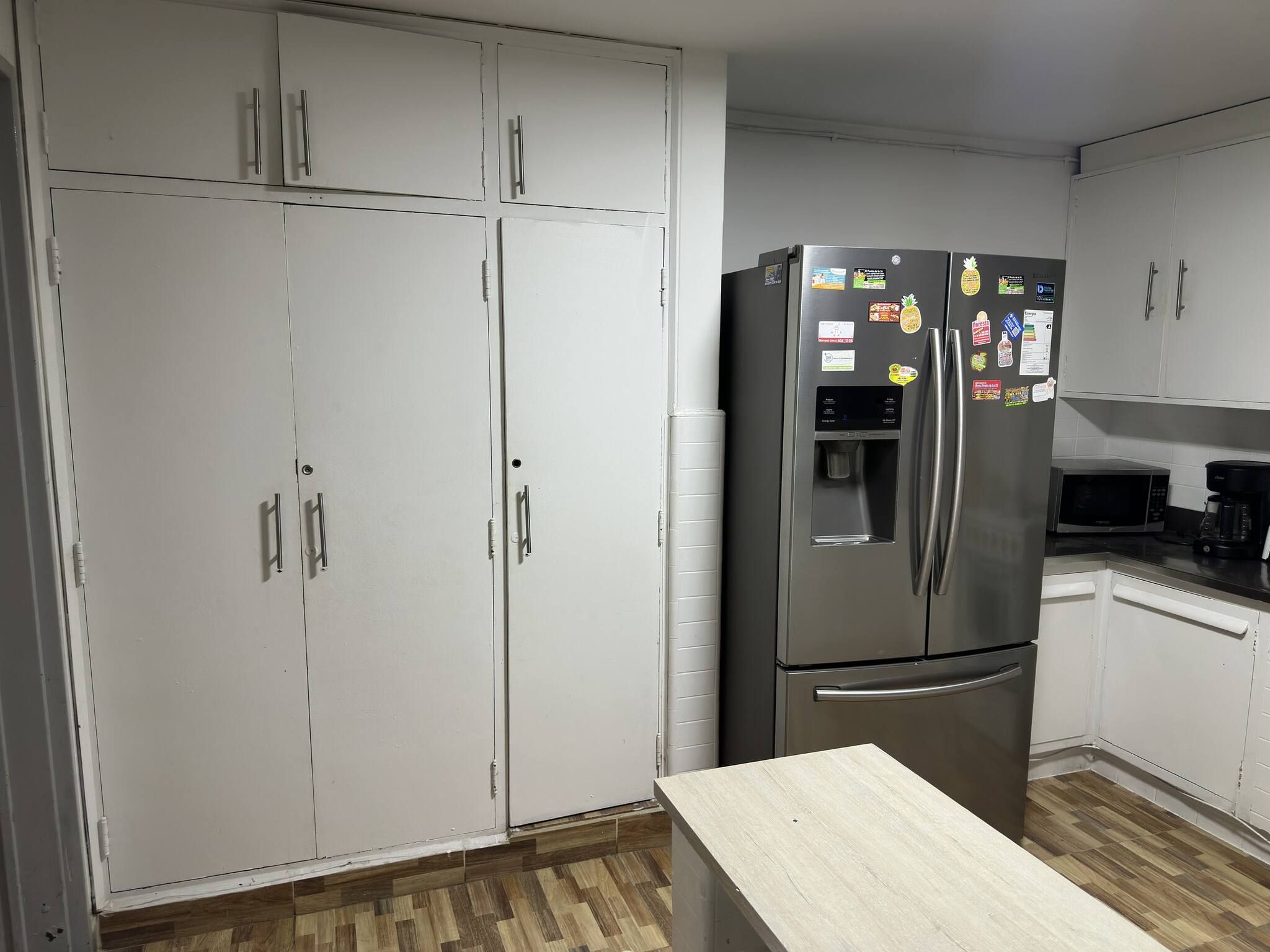 A compact kitchen with white cabinets, a stainless steel refrigerator with a water dispenser, a microwave, and a coffee maker on the countertop.