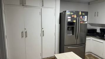 A compact kitchen with white cabinets, a stainless steel refrigerator with a water dispenser, a microwave, and a coffee maker on the countertop.