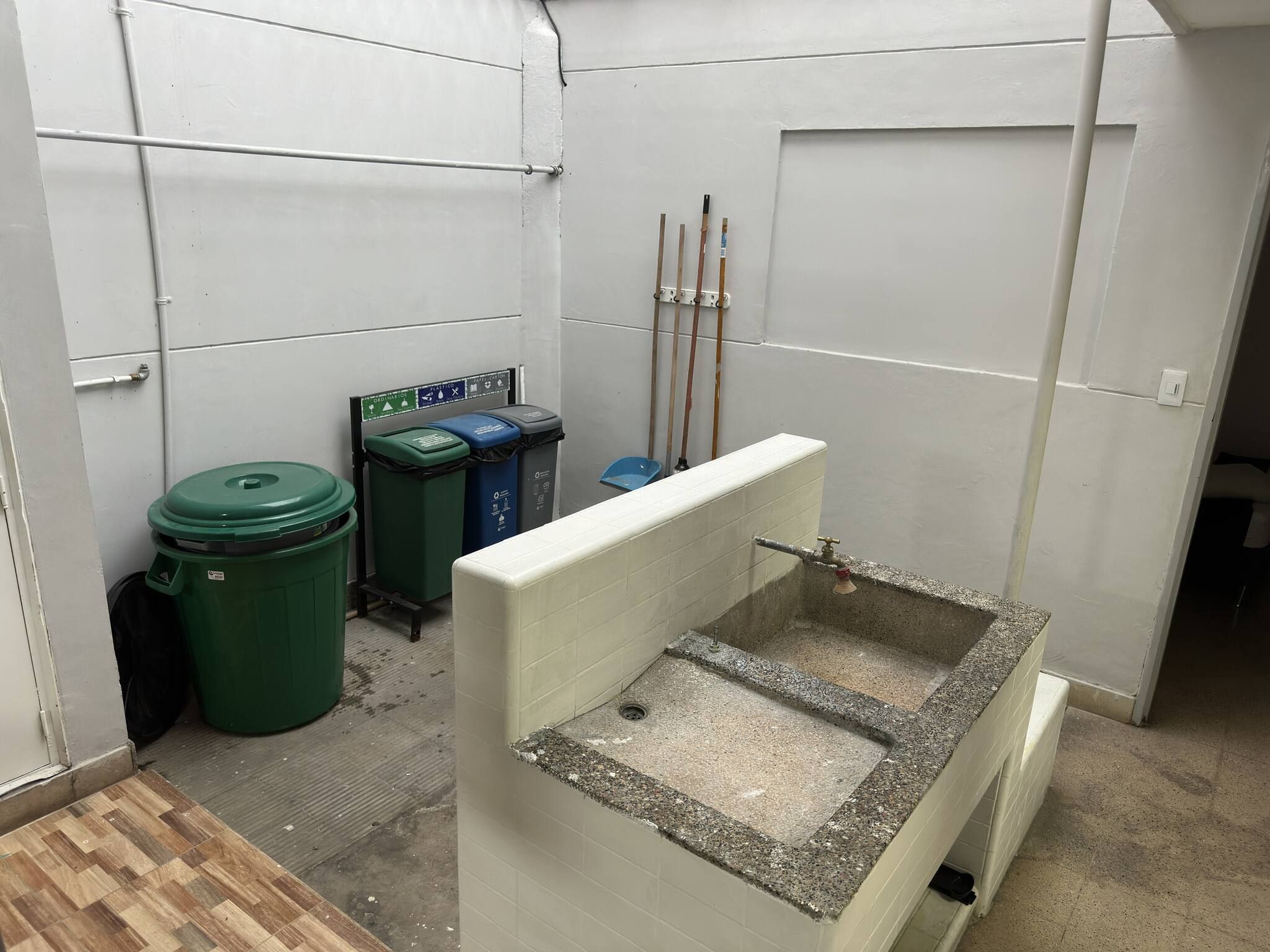 A small, enclosed bathroom with a sink, two trash bins, and a handwashing station.