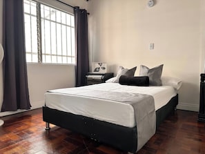 A bedroom with a bed, a nightstand, a wall clock, and a window with curtains. - Group Stay 21 Guests, Wifi 900 Mb (Medellín)