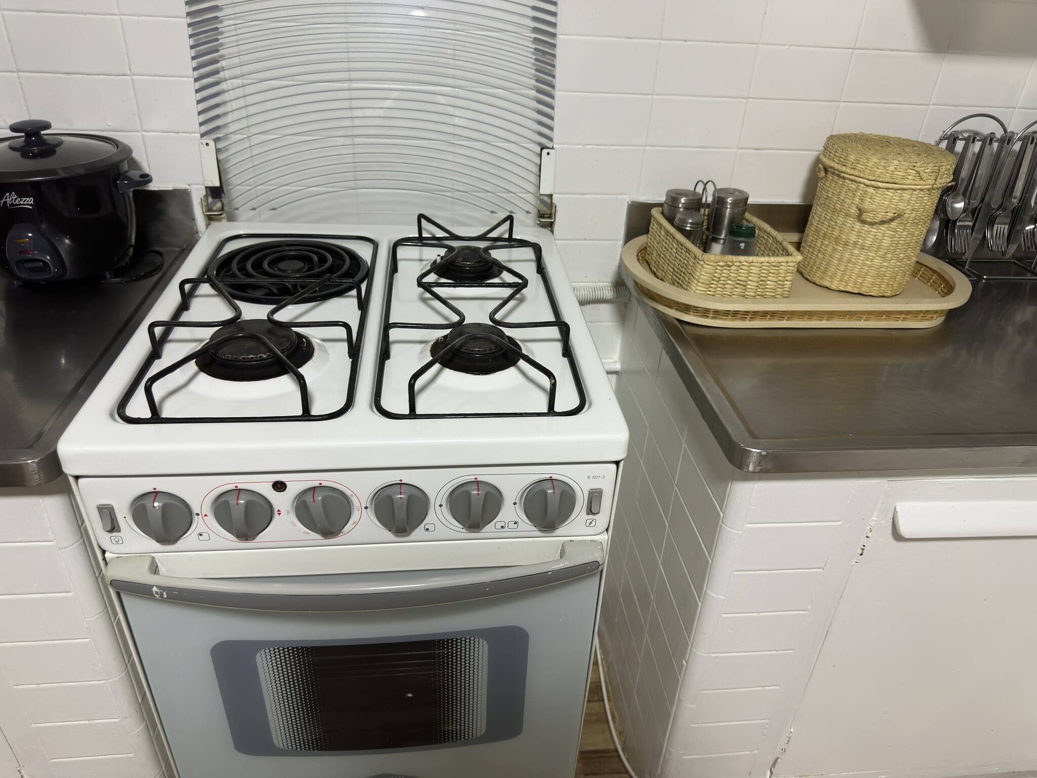 Una cocina con estufa blanca, una olla negra y una cesta de mimbre con utensilios.