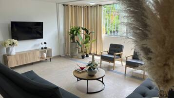 A modern living room with a flat-screen TV, a wooden console table, two black sofas, a round coffee table, and a large window with curtains.