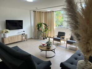 A modern living room with a flat-screen TV, a wooden console table, two black sofas, a round coffee table, and a large window with curtains. - Group Stay 21 Guests, Wifi 900 Mb (Medellín)