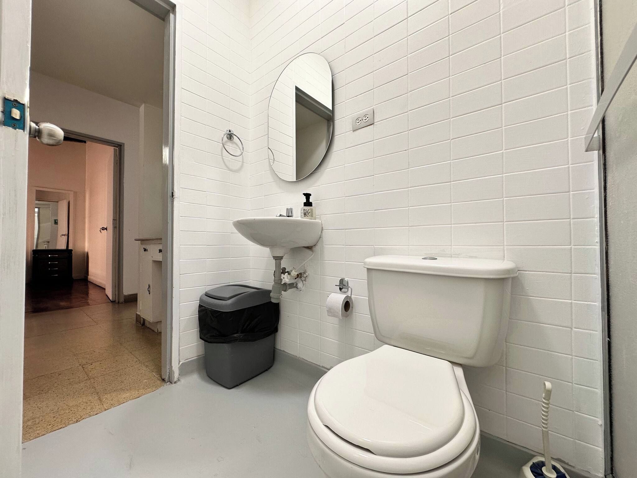 Un baño con paredes de azulejos blancos, un lavabo blanco, un inodoro y un cubo de basura.