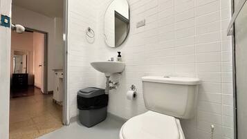 Un baño con paredes de azulejos blancos, un lavabo blanco, un inodoro y un cubo de basura.