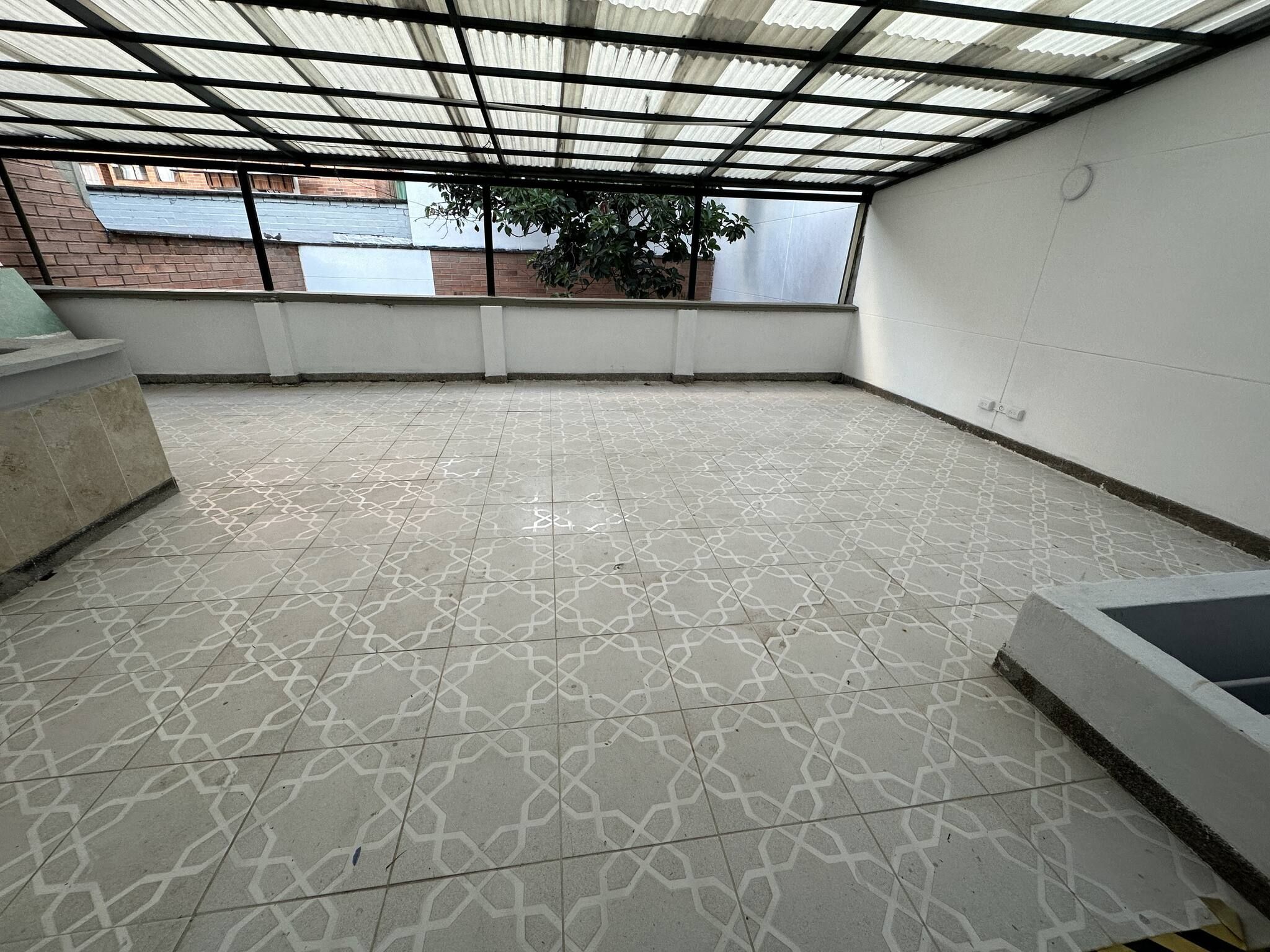 A covered outdoor area with patterned flooring, a metal roof, and a brick wall in the background.
