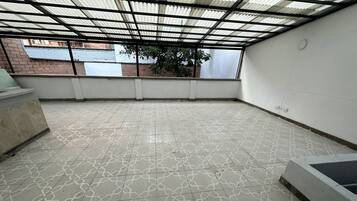 A covered outdoor area with patterned flooring, a metal roof, and a brick wall in the background.