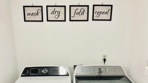 Two front-loading washing machines side by side with control panels and a wall-mounted sign above them with the words "wash," "dry," "fold," and "repeat." - Newly Renovated 3-bedroom home near Yellowstone National Park (Livingston)