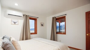 A bedroom with a bed, two windows with curtains, an air conditioner, and framed pictures on the wall. - Newly Renovated 3-bedroom home near Yellowstone National Park (Livingston)