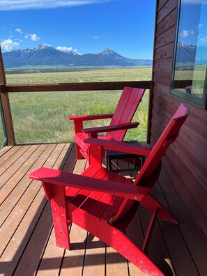 Une chaise Adirondack rouge sur une terrasse en bois, avec vue sur les montagnes.