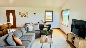 A modern living room with a grey sectional sofa, a coffee table, a TV on a wooden stand, and a dining area with a wooden table and chairs. - Newly Renovated 3-bedroom home near Yellowstone National Park (Livingston)
