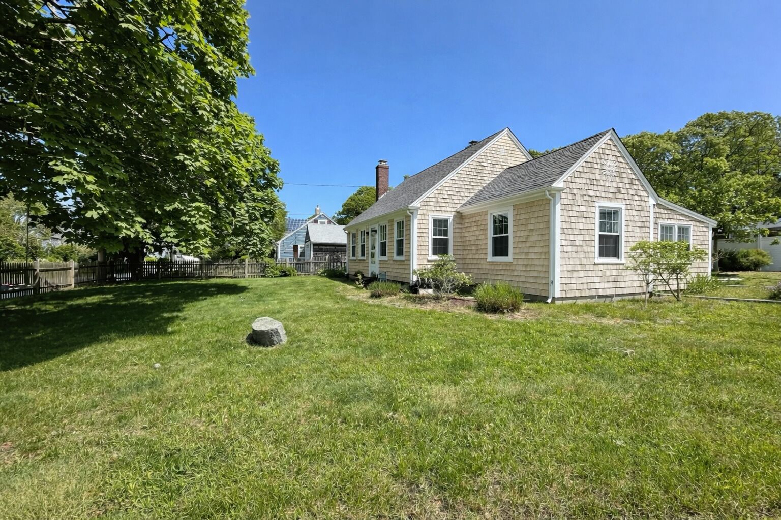 A two-story house with a well-maintained lawn and a large tree in the foreground.