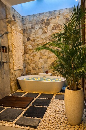 Un espace spa agrémenté d’un mur en pierre, d’une baignoire sur pieds et d’une plante en pot.