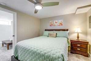 Une chambre à coucher comprenant un lit, une table de chevet, une lampe, un ventilateur de plafond et une porte.