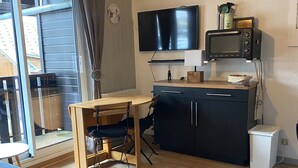 Un espacio habitable compacto con sofá, escritorio de madera, televisor, microondas y un pequeño cubo de basura.
