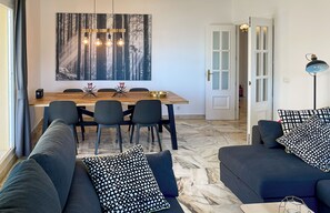 A modern living room with a dining area, featuring a wooden dining table, dark sofas, and a large abstract painting on the wall. - 139 - Modern Coastal Apartment with Pool & Sea Views in La Cala de Mijas (La Cala de Mijas)