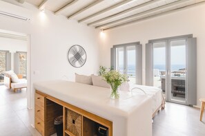 Ein modernes Schlafzimmer mit einem großen Bett, einem Holzschrank, einer Vase mit Blumen und Meerblick durch große Fenster.