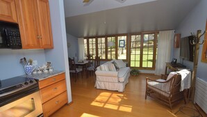 A spacious kitchen with wooden cabinets, a built-in oven, and a dining area with a sofa and chairs. - Adorable 1-bedroom cottage with AC in Shelter Island (Shelter Island)
