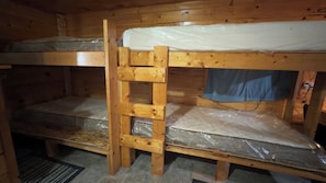 A bunk bed room with a wooden ladder, a mattress on each bed, and a blue curtain on the upper bunk.