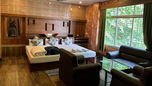 Une chambre d’hôtel avec un lit, un canapé, une chaise, une petite table et une fenêtre avec des rideaux.
