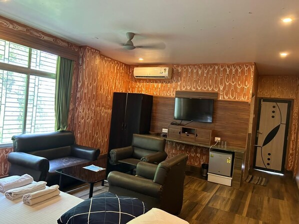 A living room with a sofa, armchairs, a TV, and a small refrigerator.