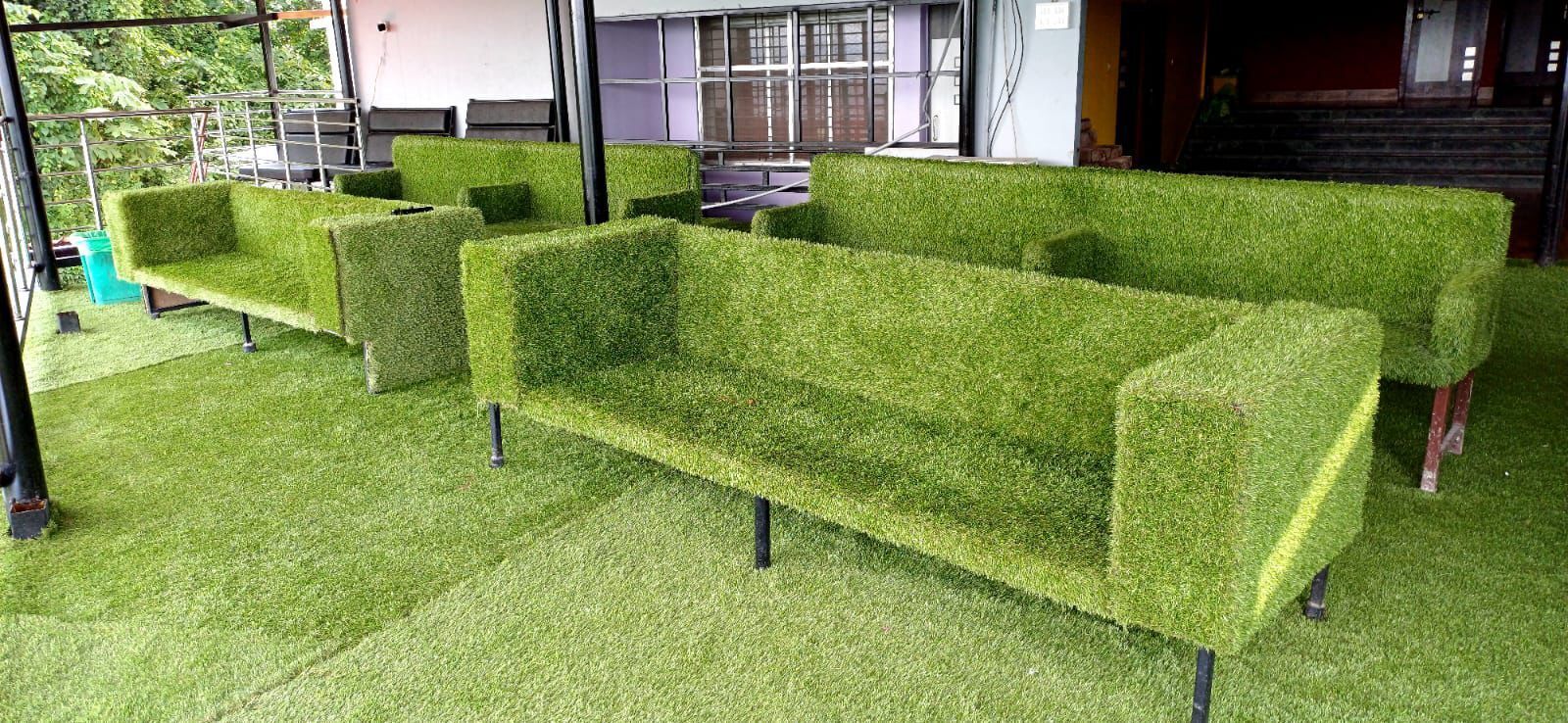 A row of green, grass-like sofas with metal legs, arranged in a row on a green carpeted floor.