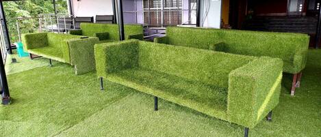 Una fila de sofás verdes, con aspecto de césped y patas metálicas, alineados sobre un suelo cubierto de alfombra verde.