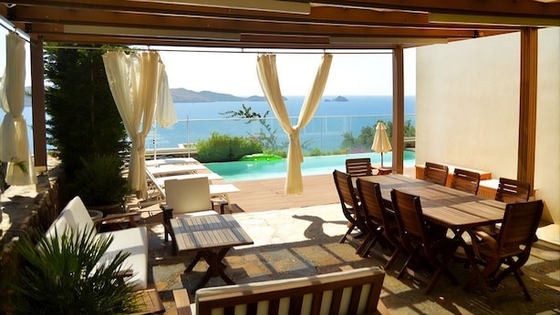 Un espacio de comedor al aire libre con techo y vistas al mar y a las montañas.