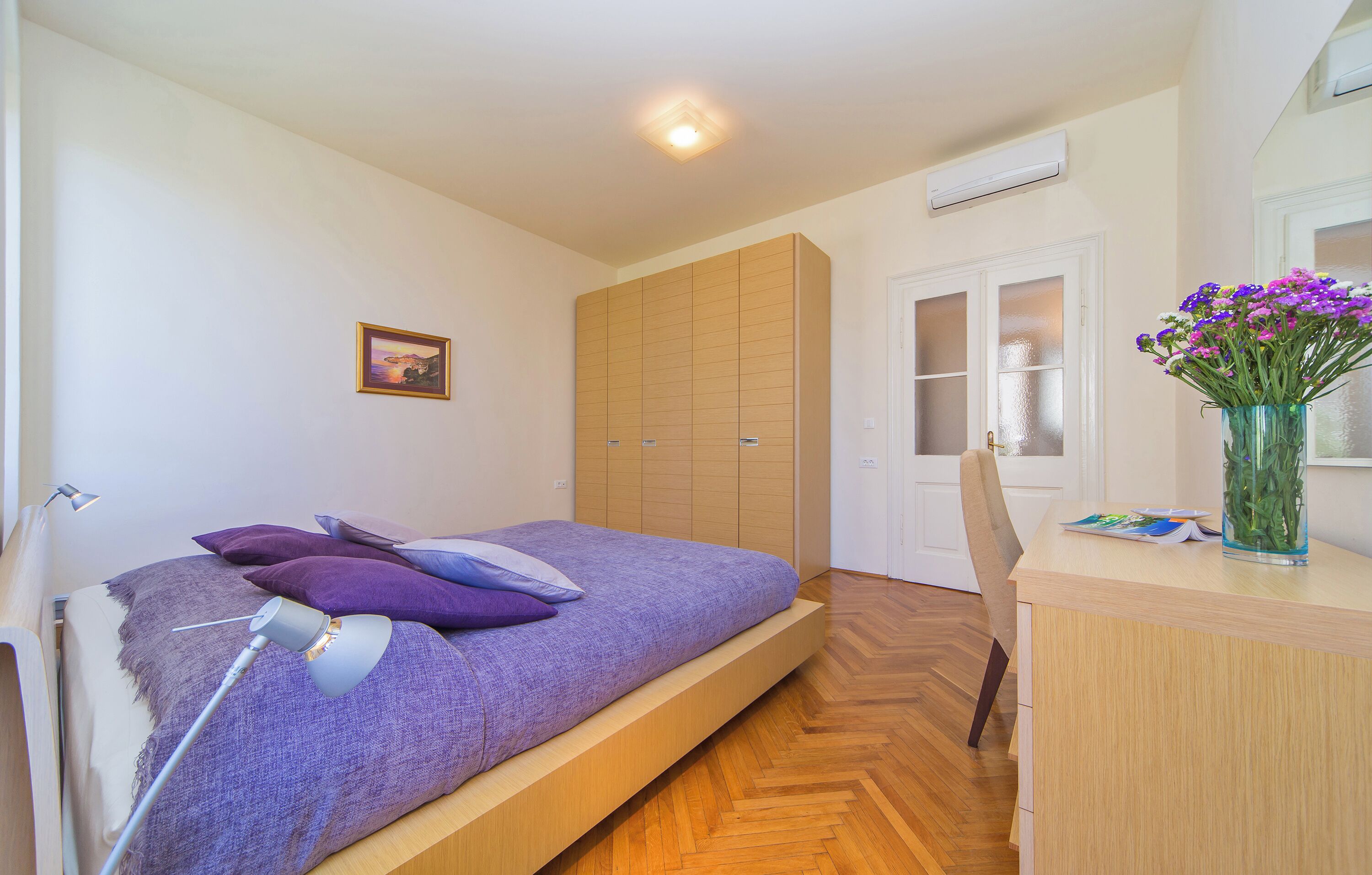 Une chambre à coucher comprenant un lit, un bureau, une chaise, une lampe, une armoire et un vase avec des fleurs.
