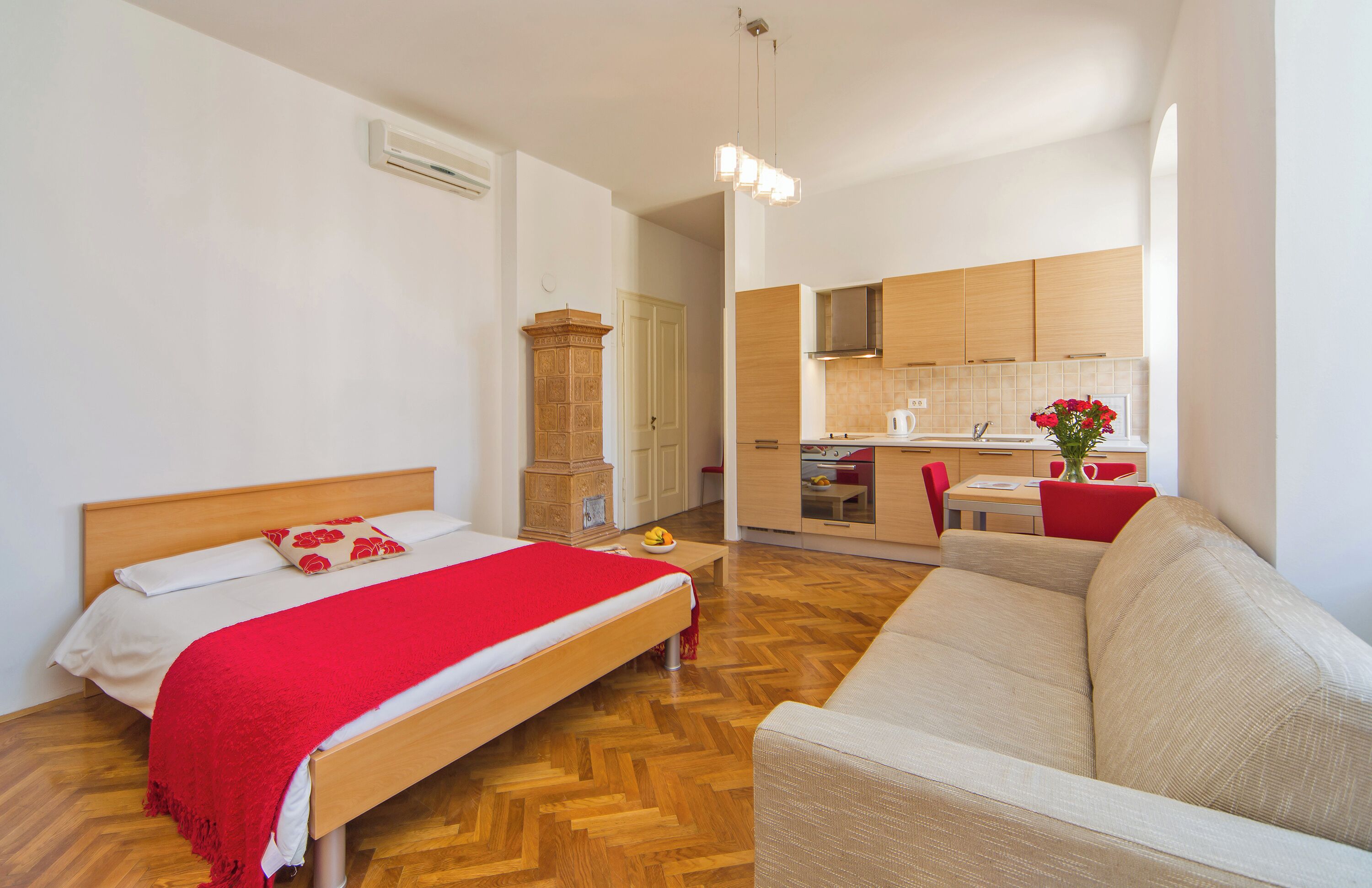 Un dormitorio con cama, una manta roja y piso de madera.