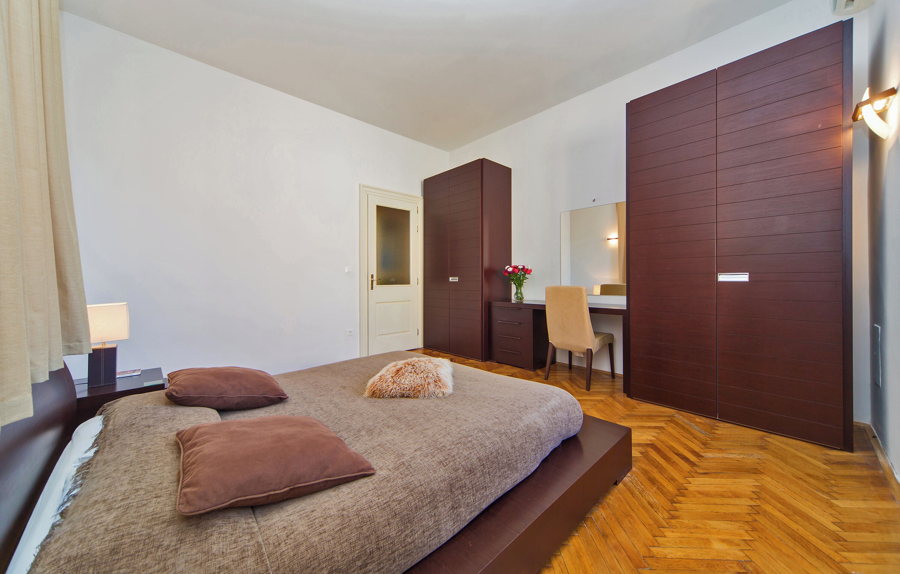A modern bedroom with a large bed, a desk, and a wardrobe.